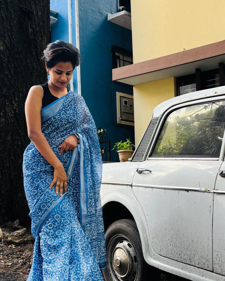 The founder of SILA Collective in a blue printed saree, standing beside a vintage car